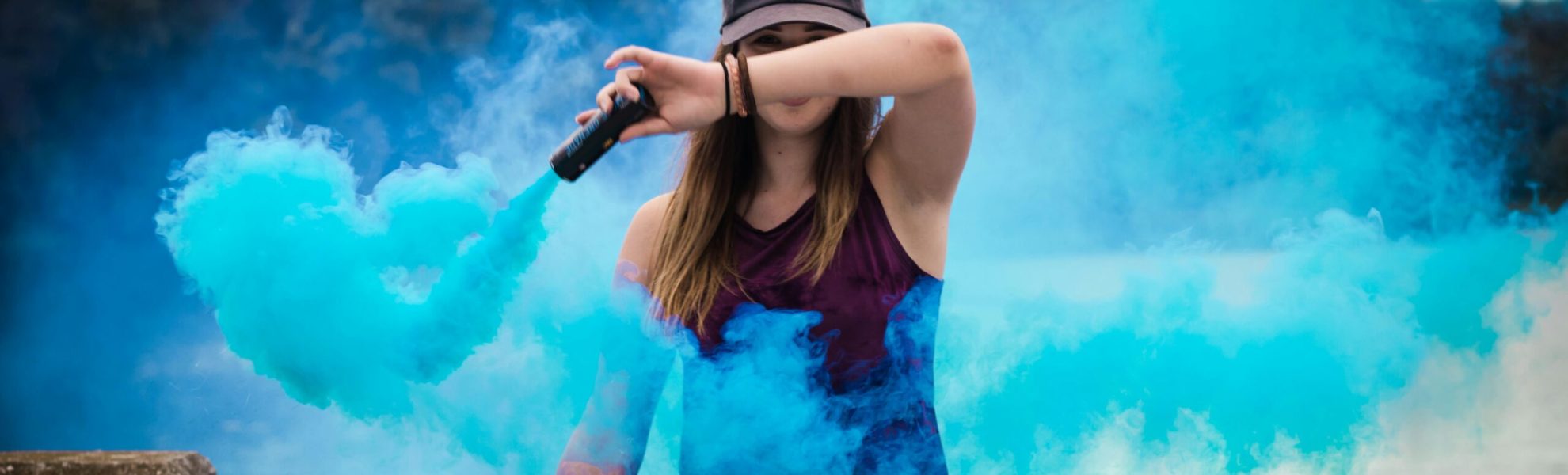 A stylish woman surrounded by bright blue smoke outdoors, creating a dynamic fashion statement.